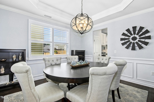 dining room featuring a notable chandelier, wainscoting, a raised ceiling, and dark wood-type flooring