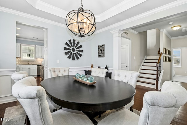 dining space featuring stairway, ornate columns, dark wood-style flooring, crown molding, and a notable chandelier