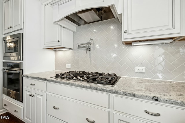 kitchen with white cabinets, light stone counters, premium range hood, and stainless steel appliances