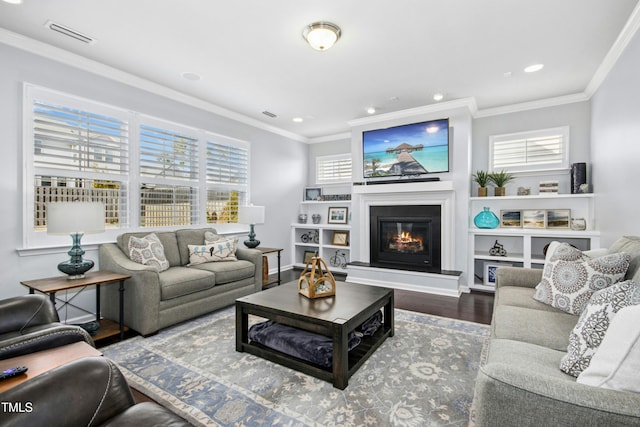 living area with visible vents, a glass covered fireplace, wood finished floors, recessed lighting, and crown molding