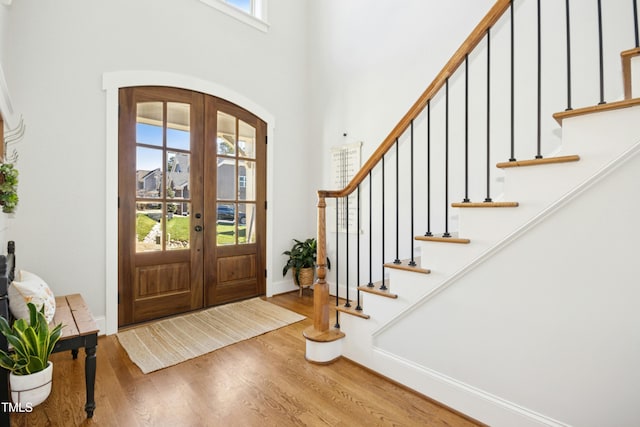 entryway with wood finished floors, french doors, arched walkways, baseboards, and stairs