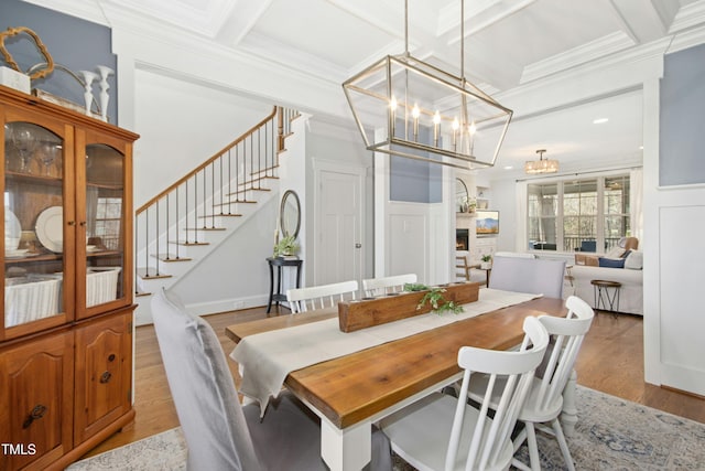 dining area featuring coffered ceiling, light wood-style flooring, ornamental molding, stairs, and a chandelier