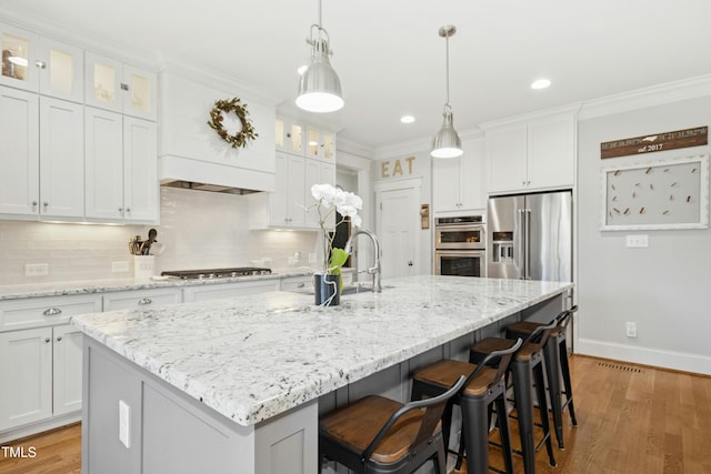 kitchen featuring a kitchen island with sink, a sink, ornamental molding, appliances with stainless steel finishes, and backsplash