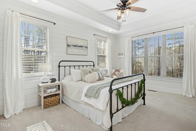 carpeted bedroom featuring a raised ceiling, multiple windows, visible vents, and ornamental molding