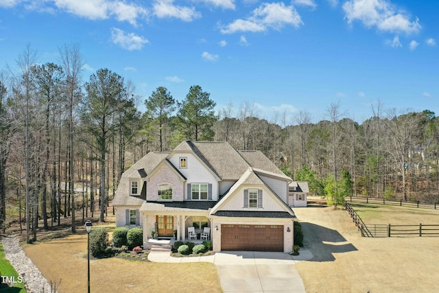 view of front of property with fence, a wooded view, driveway, a porch, and a garage