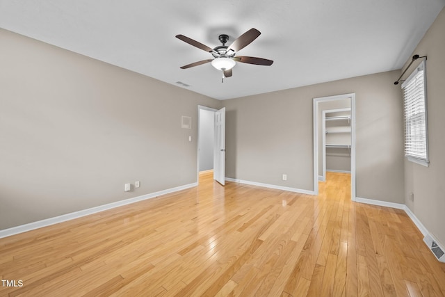 unfurnished bedroom with a spacious closet, visible vents, light wood-type flooring, and baseboards