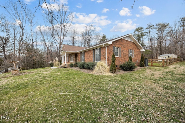 view of side of home featuring brick siding, a lawn, and fence