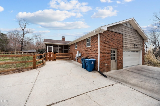 view of side of property with fence, a sunroom, concrete driveway, a garage, and brick siding