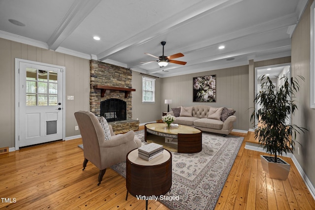 living room featuring beamed ceiling, visible vents, light wood-style flooring, a stone fireplace, and baseboards