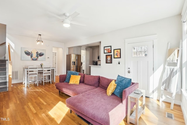 living area featuring light wood-type flooring, visible vents, and stairs