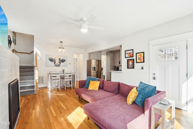 living area with stairway, visible vents, light wood finished floors, a fireplace, and ceiling fan