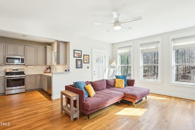 living room with light wood finished floors, visible vents, baseboards, and ceiling fan