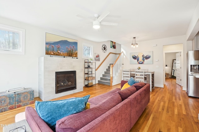 living area with a tiled fireplace, stairway, and light wood-style flooring