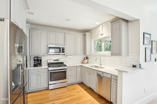 kitchen with light wood finished floors, gray cabinetry, stainless steel appliances, and a sink