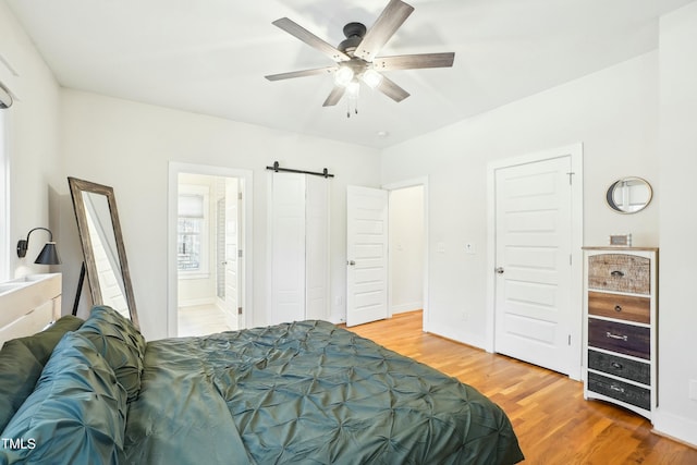 bedroom featuring wood finished floors, baseboards, ensuite bath, ceiling fan, and a barn door