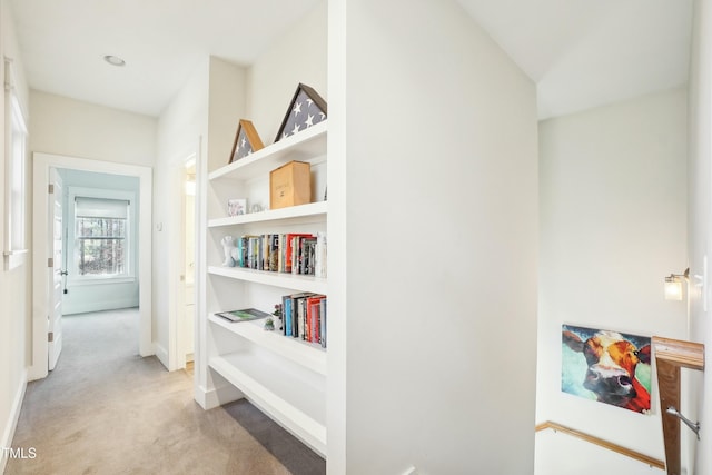 hallway featuring light colored carpet and baseboards