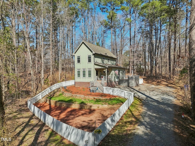 view of front of property featuring a porch, fence, a wooded view, and a shingled roof