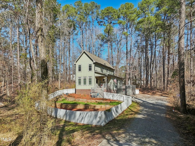 view of front of property with a wooded view, board and batten siding, fence, covered porch, and driveway