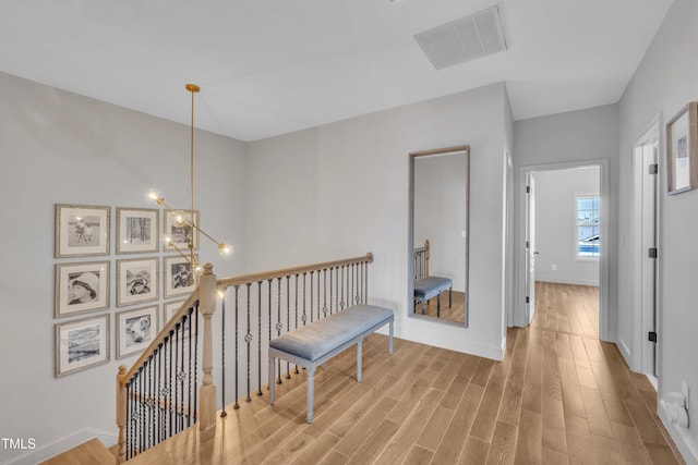 corridor featuring visible vents, baseboards, an upstairs landing, wood finished floors, and a notable chandelier