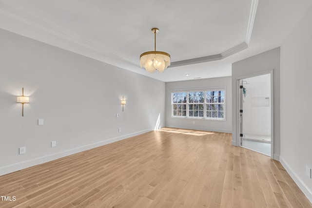 spare room featuring a tray ceiling, light wood-style flooring, crown molding, and baseboards