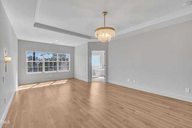 empty room featuring baseboards, light wood finished floors, a tray ceiling, ornamental molding, and a chandelier