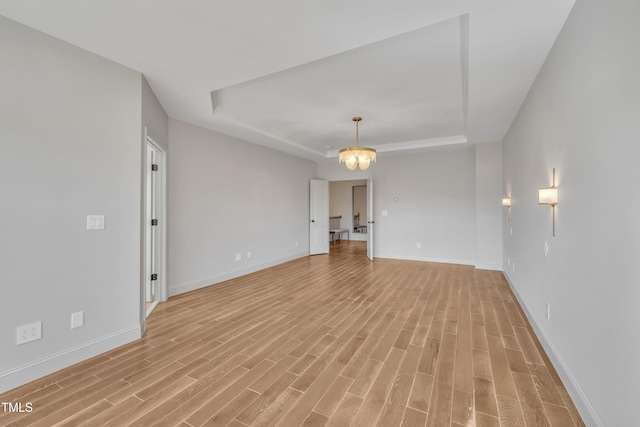 empty room with light wood finished floors, an inviting chandelier, baseboards, and a tray ceiling