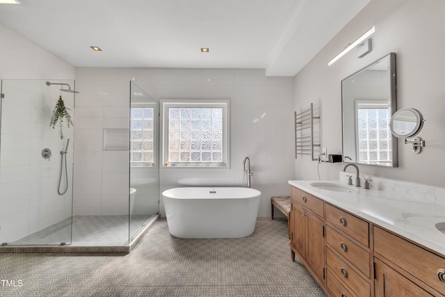 bathroom with a sink, a tile shower, tile walls, double vanity, and a freestanding bath