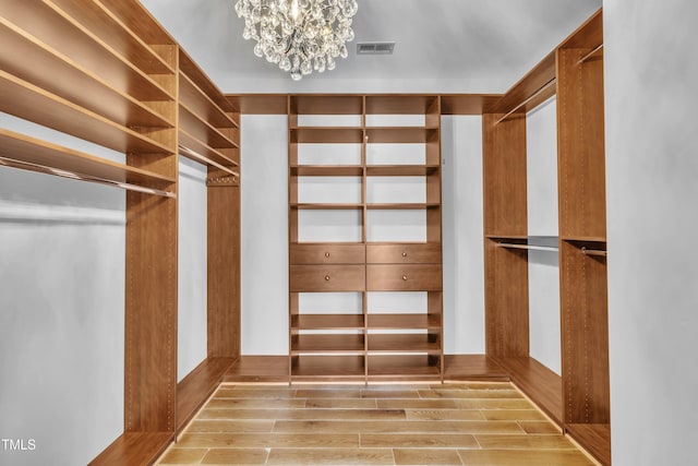 walk in closet with an inviting chandelier, wood finished floors, and visible vents