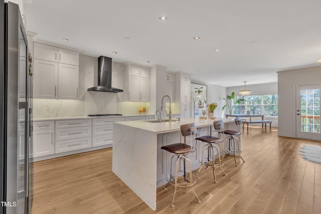 kitchen featuring a sink, gas stovetop, light wood-style floors, wall chimney exhaust hood, and decorative backsplash