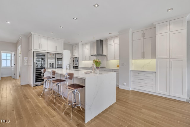 kitchen featuring light wood finished floors, white cabinets, appliances with stainless steel finishes, a kitchen breakfast bar, and wall chimney exhaust hood