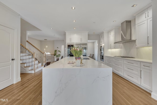 kitchen featuring light wood-style flooring, appliances with stainless steel finishes, wall chimney exhaust hood, and decorative backsplash