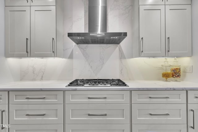 kitchen featuring light stone counters, decorative backsplash, stainless steel gas stovetop, white cabinets, and wall chimney exhaust hood