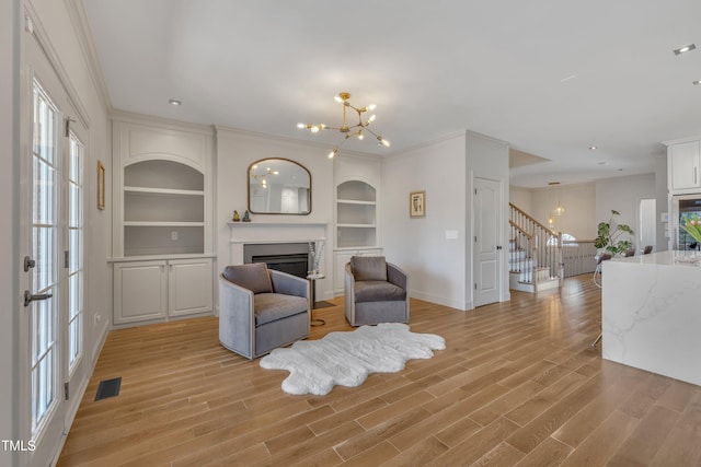 living area featuring light wood finished floors, visible vents, stairs, a fireplace, and a notable chandelier