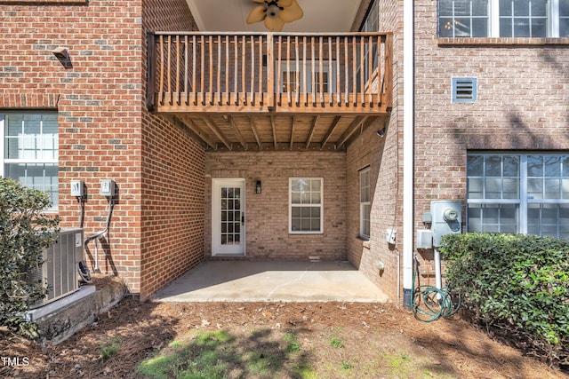 view of exterior entry featuring brick siding, a balcony, cooling unit, and a patio