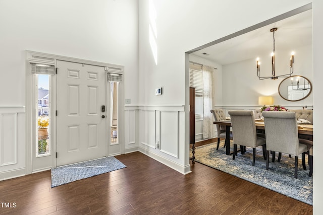 foyer with a wainscoted wall, a notable chandelier, dark wood-style floors, and a decorative wall