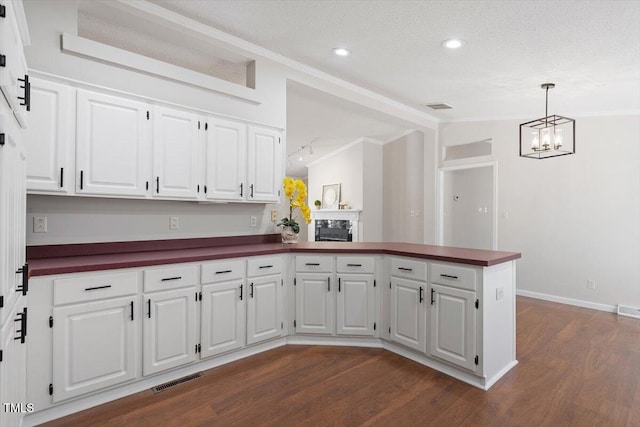 kitchen featuring dark countertops, lofted ceiling, a peninsula, dark wood-style floors, and white cabinets