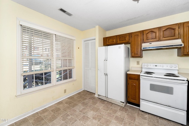 kitchen with visible vents, under cabinet range hood, light countertops, brown cabinets, and white appliances