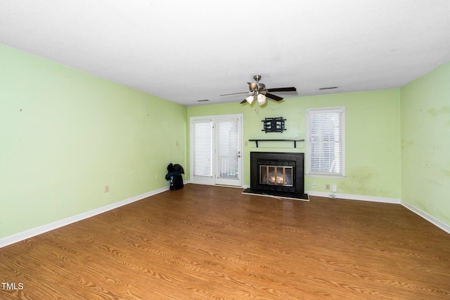 unfurnished living room with a glass covered fireplace, a ceiling fan, baseboards, and wood finished floors