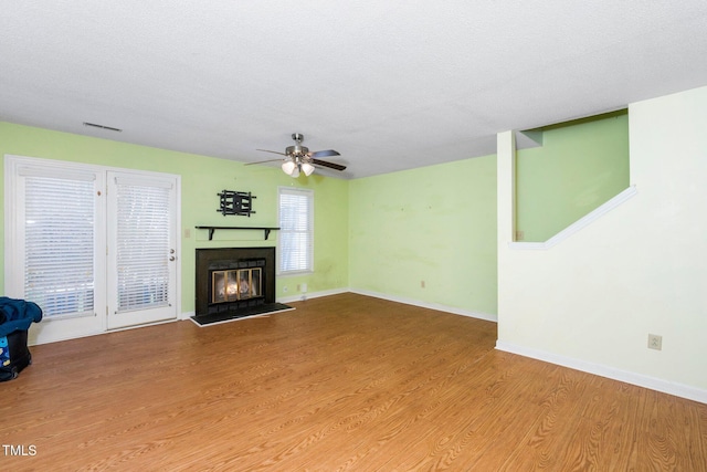 unfurnished living room with visible vents, baseboards, wood finished floors, a glass covered fireplace, and a ceiling fan