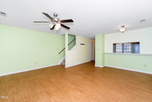 unfurnished living room featuring wood finished floors, baseboards, visible vents, ceiling fan, and stairs