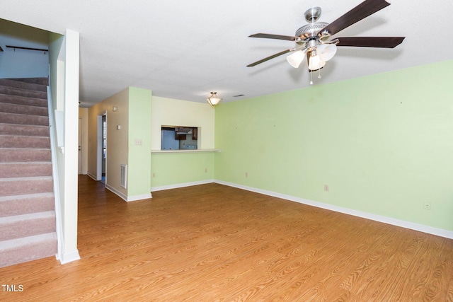 unfurnished living room featuring ceiling fan, stairway, baseboards, and wood finished floors