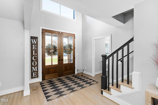 foyer entrance featuring a high ceiling, stairway, wood finished floors, and baseboards