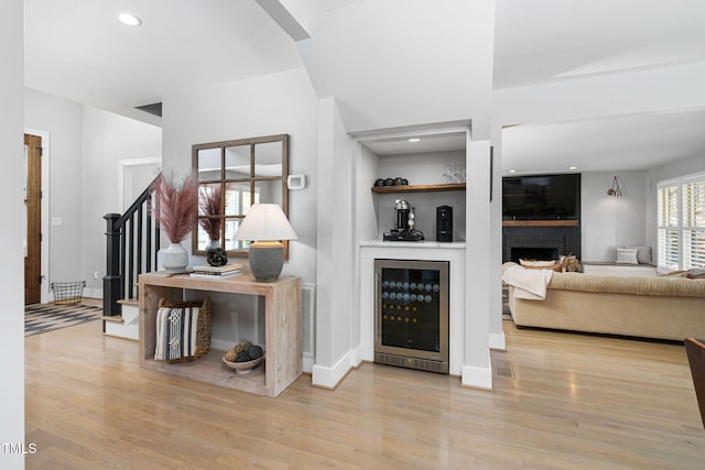 living area with beverage cooler, a brick fireplace, stairs, and wood finished floors