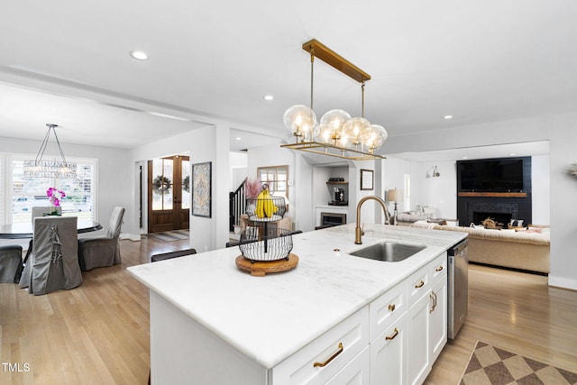 kitchen with light wood finished floors, a fireplace, a sink, dishwasher, and open floor plan