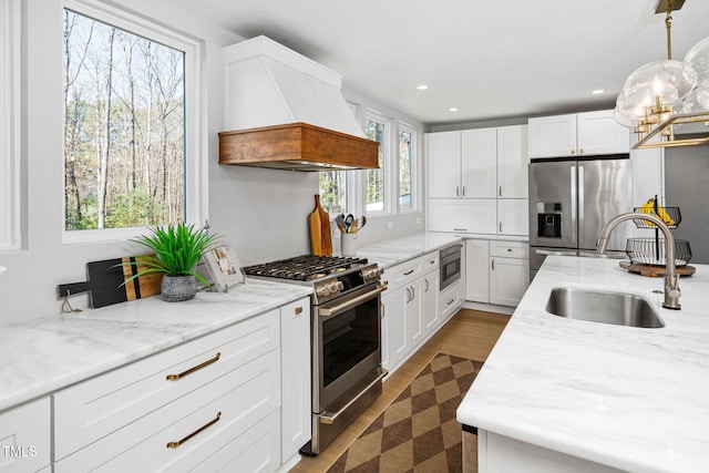 kitchen featuring white cabinets, premium range hood, appliances with stainless steel finishes, and a sink