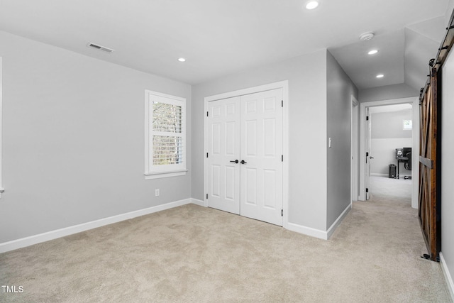 unfurnished bedroom featuring visible vents, baseboards, light colored carpet, a barn door, and recessed lighting