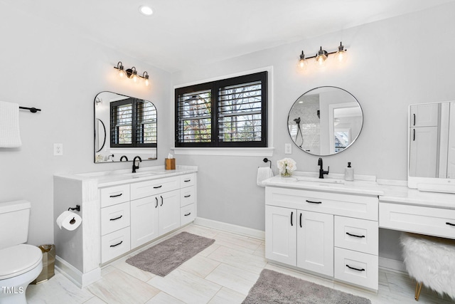 full bathroom featuring a sink, baseboards, toilet, and two vanities