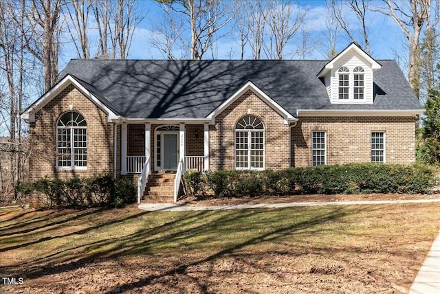 view of front of property featuring brick siding, a front lawn, and a shingled roof