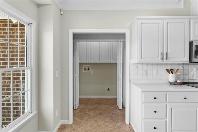 kitchen featuring backsplash, crown molding, baseboards, light countertops, and white cabinetry