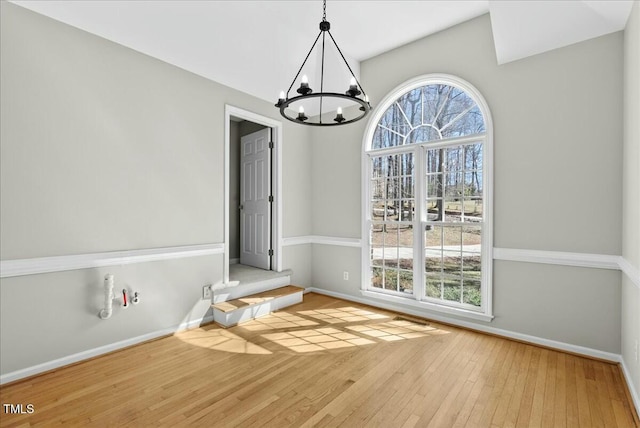 unfurnished dining area featuring hardwood / wood-style flooring, baseboards, and a chandelier